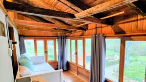 Quarto de cabana de madeira com uma cama, uma escrivaninha e grandes janelas.
