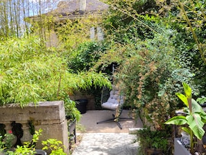 Ein Garten mit einem Kiesweg, der zu einer Sitzgelegenheit führt, umgeben von üppiger Vegetation und einem Gebäude im Hintergrund.