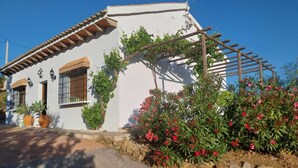 A white building with a tiled roof, a stone wall, and a wooden pergola. - Peaceful Gated Home, Fast Wifi for Remote Work, Private Pool, BBQ, Kids Area (Casabermeja)
