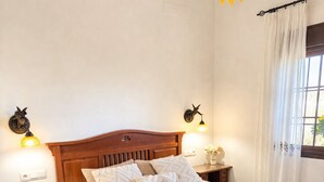 A neatly made bed with a white duvet and decorative pillows, wooden headboard, bedside tables with lamps, and a window with curtains. - Peaceful Gated Home, Fast Wifi for Remote Work, Private Pool, BBQ, Kids Area (Casabermeja)