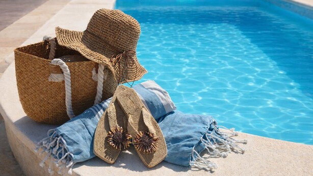 A poolside setting with a woven basket, a straw hat, and a pair of sandals. - Peaceful Gated Home, Fast Wifi for Remote Work, Private Pool, BBQ, Kids Area (Casabermeja)