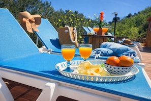 A sun lounger with a tray of food and drinks, a woven bag, and a blue and white patterned bowl.