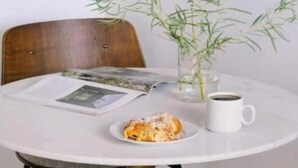 A round dining table with a white tablecloth, a plate of food, a cup of coffee, and a small potted plant.