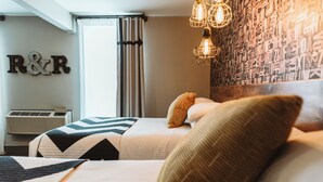 Une chambre d’hôtel avec deux lits, un climatiseur fixé au mur, un rideau et un mur orné des lettres « R » et « R ».