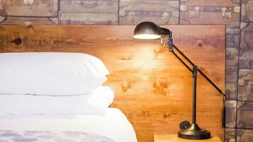 Uma cama com roupa de cama branca, uma cabeceira de madeira e uma luminária de mesa preta sobre um criado-mudo de madeira.