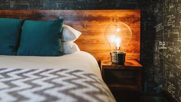 Een bed met een geborduurde spreideken, teal kussens en een houten hoofdeinde met een brandende lamp.