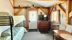 Una habitación con literas, cómoda, mesa y puerta que da a otra habitación.