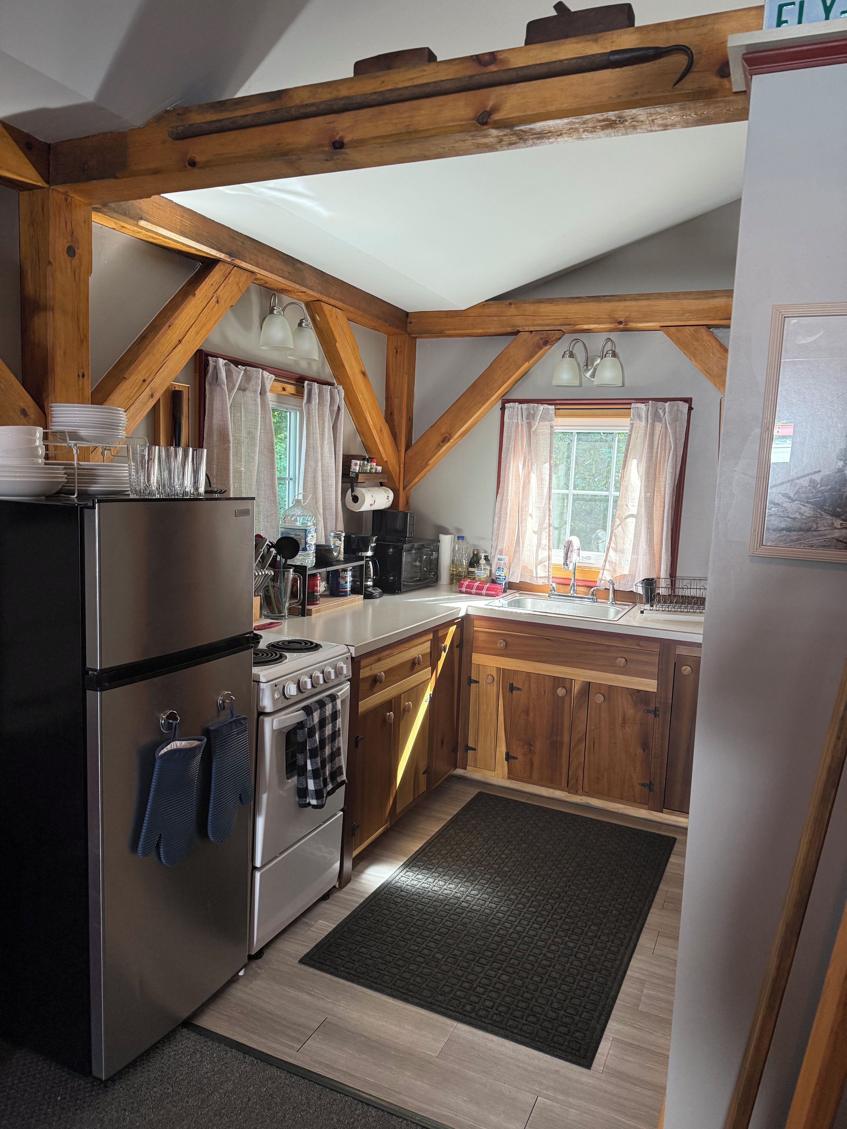 A kitchen with wooden beams, a stainless steel refrigerator, a stove, and a sink.