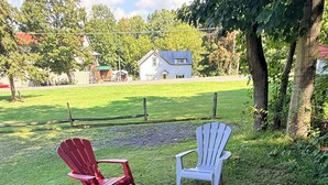 Ett grönområde med gräs, Adirondack-stolar, en eldstad och en träpall.