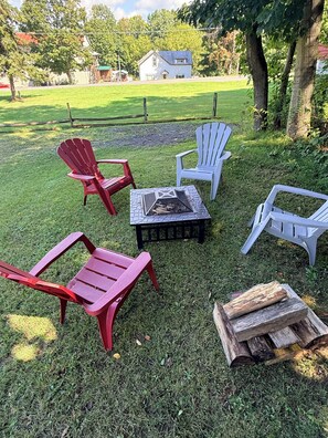 En græsplæne med Adirondack-stole, bålsted og en træpalle.
