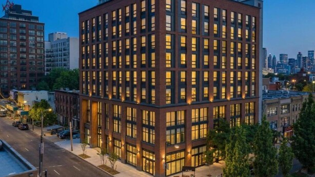 A multi-story building with a grid of windows, surrounded by other buildings and a street.