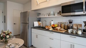 A modern kitchen with a stainless steel refrigerator, a microwave, and a variety of food items on the counter.