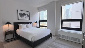 Una camera da letto moderna con un letto grande, due comodini con lampade, una finestra vista edifici e un termosifone sotto la finestra.