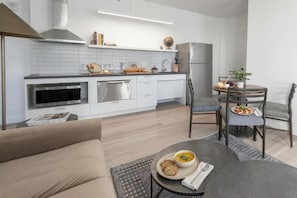 Une cuisine moderne avec des armoires blanches, un four encastré et un coin repas comprenant une table ronde et des chaises.