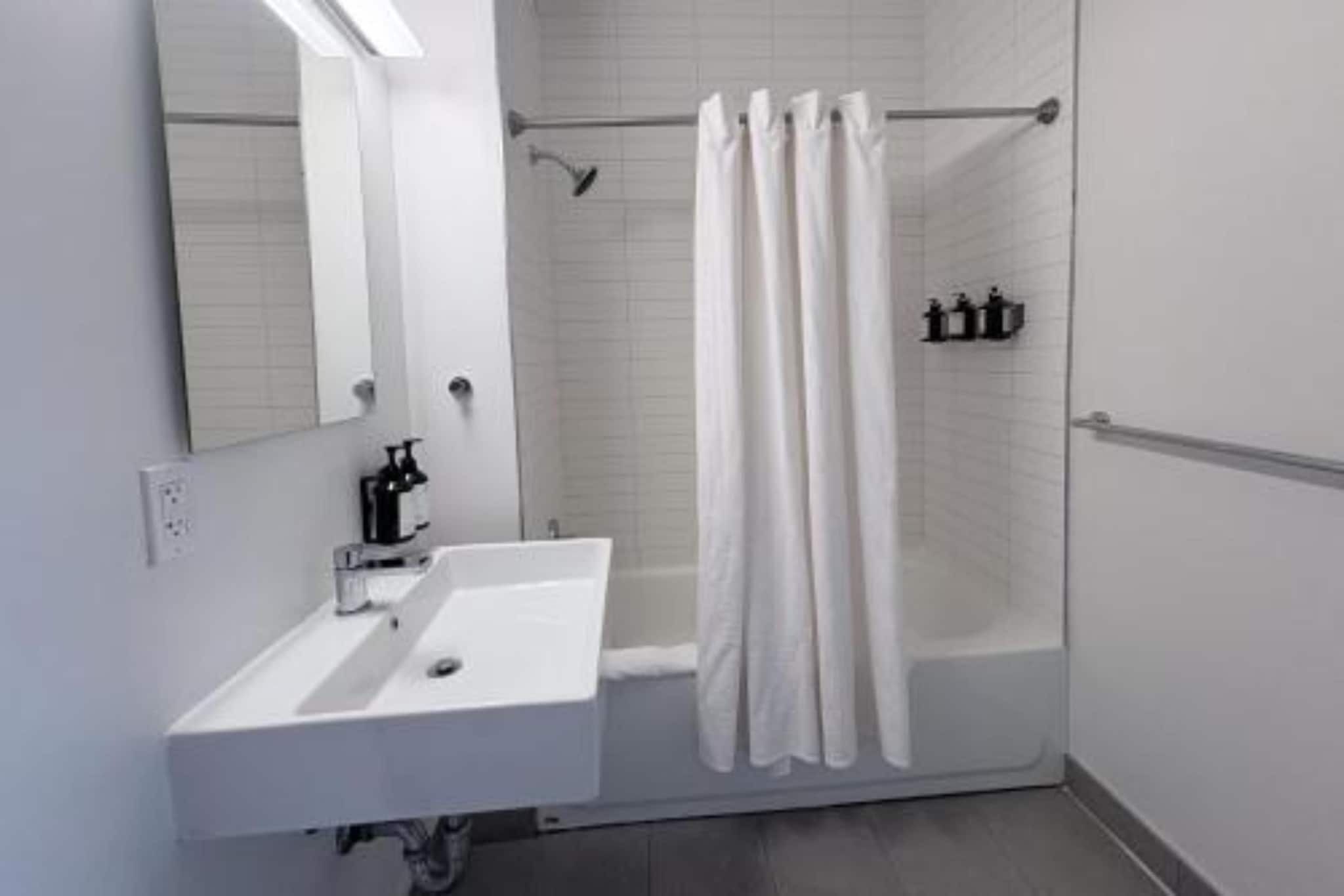 A modern bathroom with a white sink, mirror, and shower curtain.