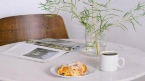 Un tavolo rotondo con una tazza bianca, un piatto con del cibo e una rivista. Una pianta di bambù è in un vaso di vetro sul tavolo.