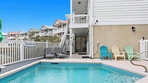 A swimming pool with a shallow pool area sign, a covered deck, and outdoor chairs. - Sunset Serenity marsh view w/pool (North Myrtle Beach)