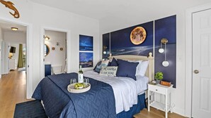 A bedroom with a bed, a nightstand, a wall clock, and a decorative wall piece. - Sunset Serenity marsh view w/pool (North Myrtle Beach)