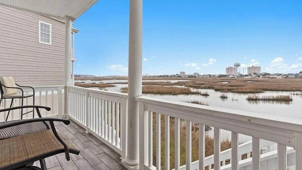 A covered porch with a view of a marshy landscape and distant buildings. - Sunset Serenity marsh view w/pool (North Myrtle Beach)