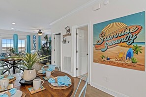 A dining area with a wooden table set for a meal, a wall with a 'Sunrise Serenity' mural, and a 'BEAUTY' sign. - 5 BR WaterFront Pool/Hottub/Elevator Sleeps 16 (North Myrtle Beach)