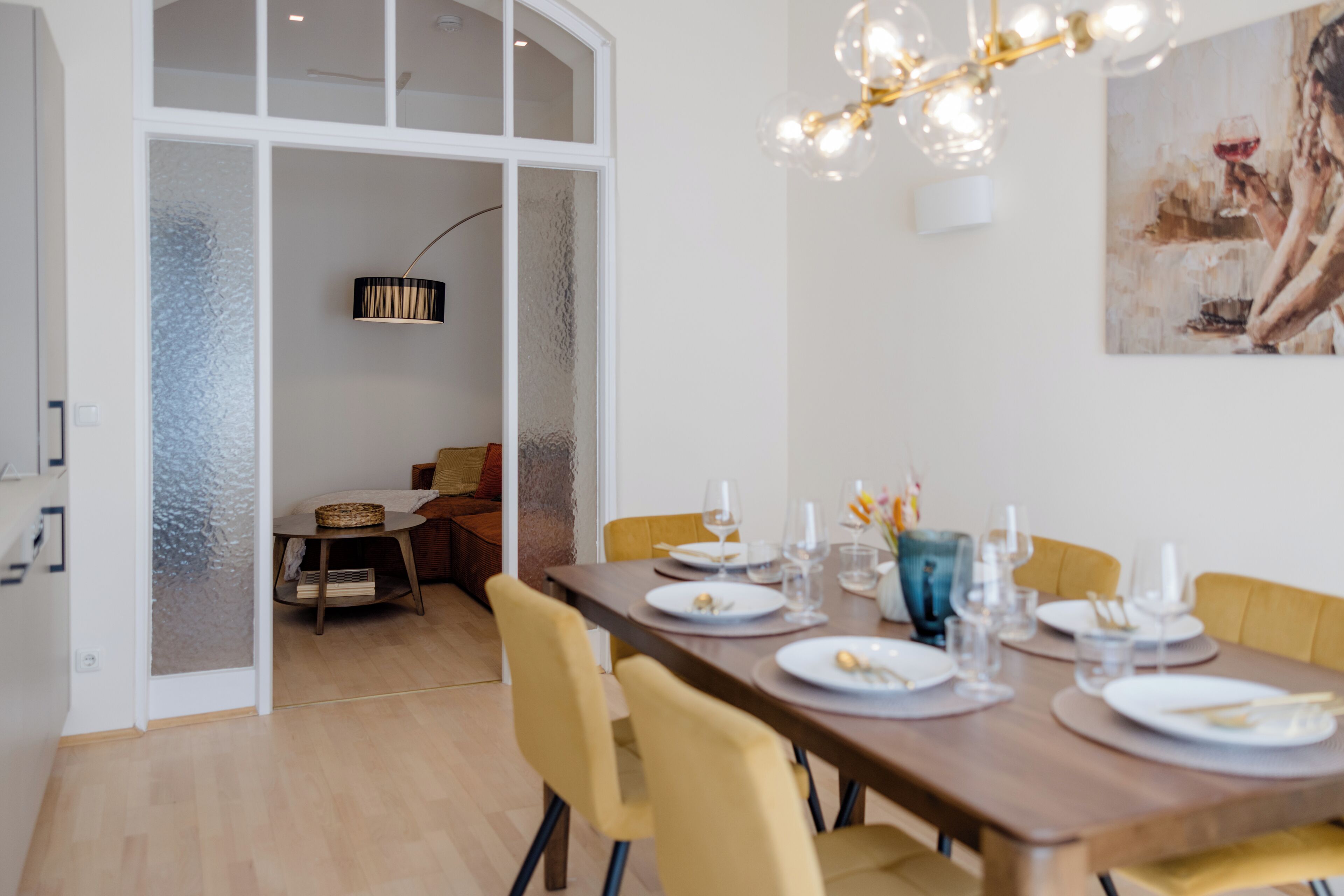 Un coin repas avec une table en bois dressée pour six personnes, des chaises jaunes et un lustre moderne.