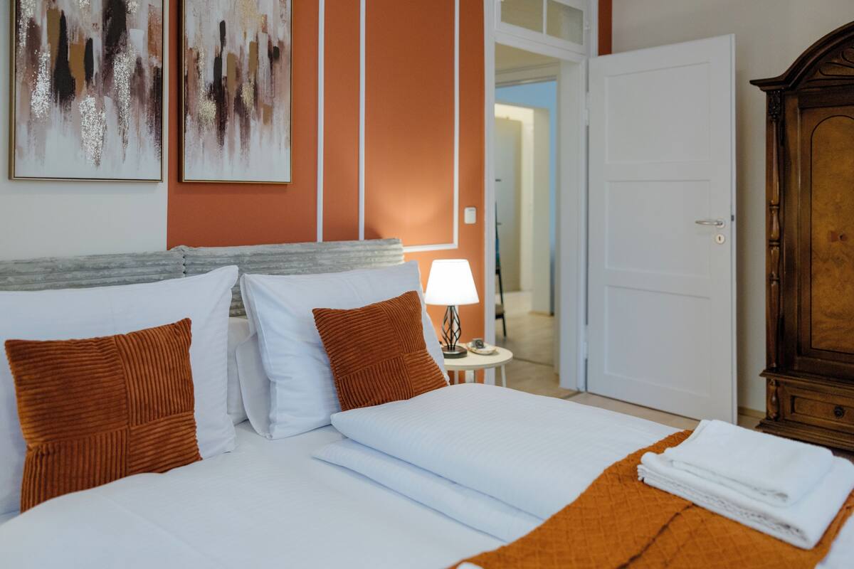 Ein Hotelzimmer mit einem Bett, Kissen, einer Lampe, einem Holzschrank und Kunstwerken an der Wand.