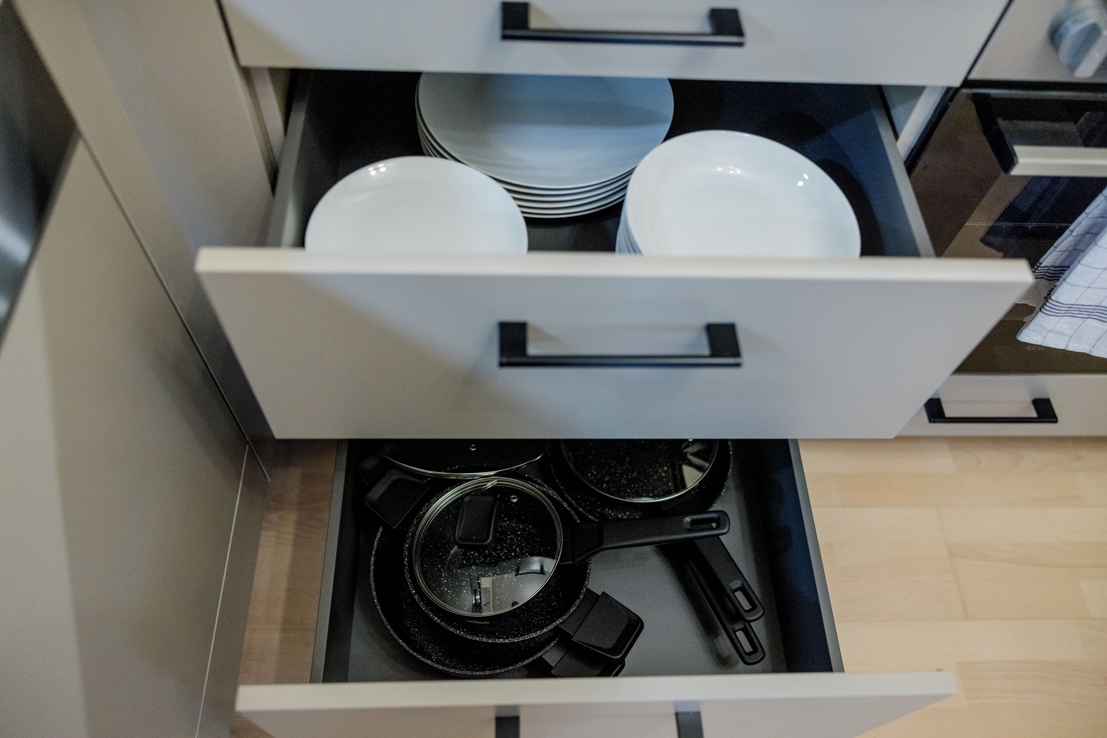 Un tiroir de cuisine contenant des assiettes blanches, des bols et une poêle.