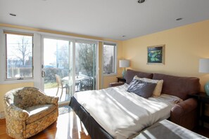 A bedroom with a bed, a chair, a table, and a view through a sliding door. - East End Studio With Private Beach Access (Provincetown)