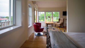 Une chambre d’hôtel avec un lit, une chaise rouge, un bureau et une vue sur la verdure.