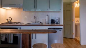 Une cuisine moderne avec des meubles blancs, un four encastré, une machine à café et un comptoir-bar en bois avec des tabourets.