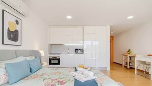 A modern bedroom with a bed, a small kitchenette, and a desk area. - 3 Stylish Flats w/ Balcony & Garage by HostWise (Porto)