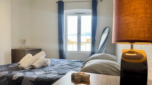 Un dormitorio con cama, una mesita de noche con lámpara, una ventana con cortinas y vistas al exterior.