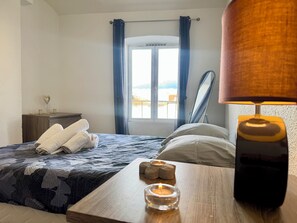 Une chambre à coucher avec un lit, une table de chevet avec une lampe, une fenêtre avec des rideaux et une vue sur l’extérieur.