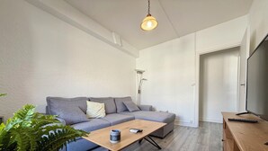 Una sala de estar moderna con un sofá gris, una mesa de centro de madera, una planta en maceta y un televisor sobre un mueble de madera.