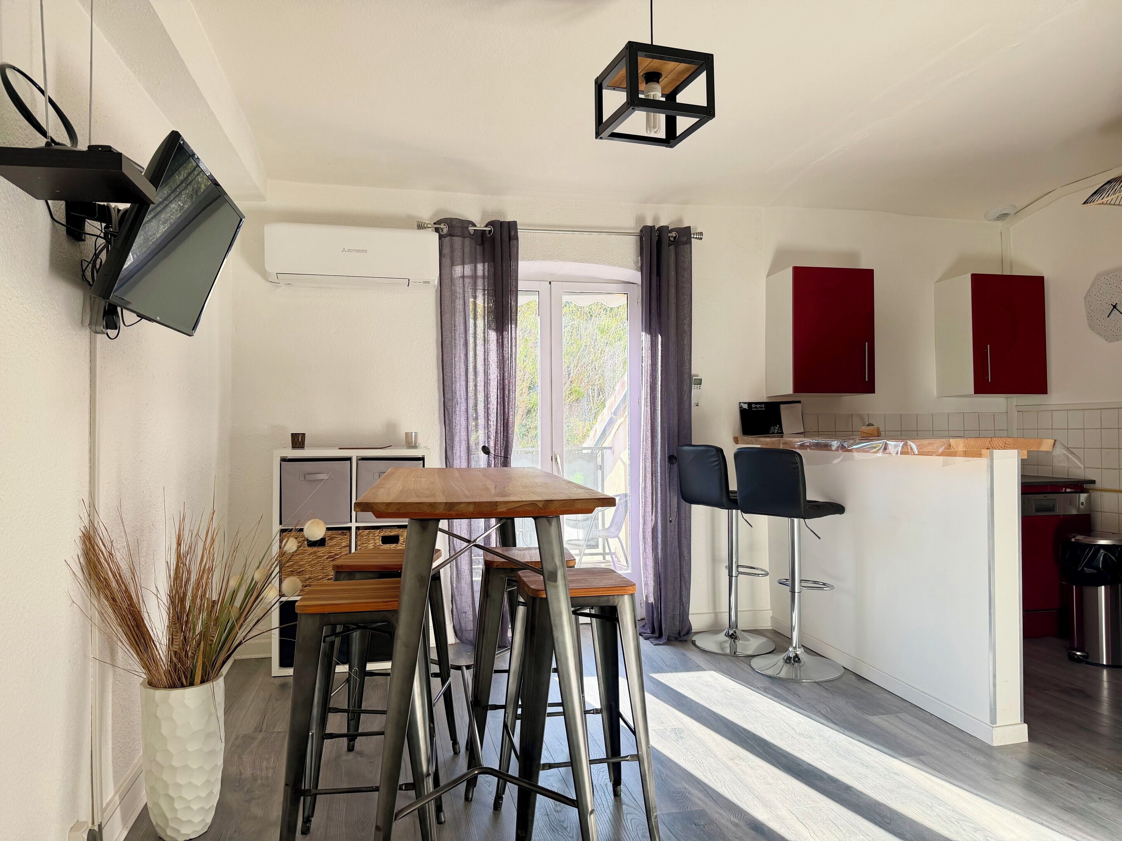 Een moderne keuken met een eethoek, barstoelen en een aan de muur bevestigde televisie.