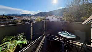 Un balcón con mesa y sillas, con vistas a un pueblo y colinas.