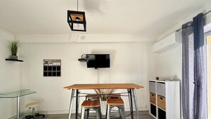Una cocina moderna con una mesa de madera, dos taburetes de bar, una lámpara colgante, un televisor montado y una planta.