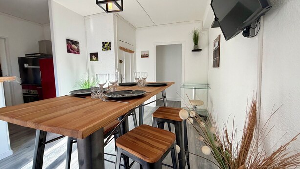 Una cocina moderna con una mesa de madera lista para comer, una lámpara colgante y un televisor montado.