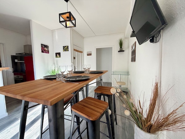 A modern kitchen with a wooden table set for dining, a hanging light fixture, and a mounted television.