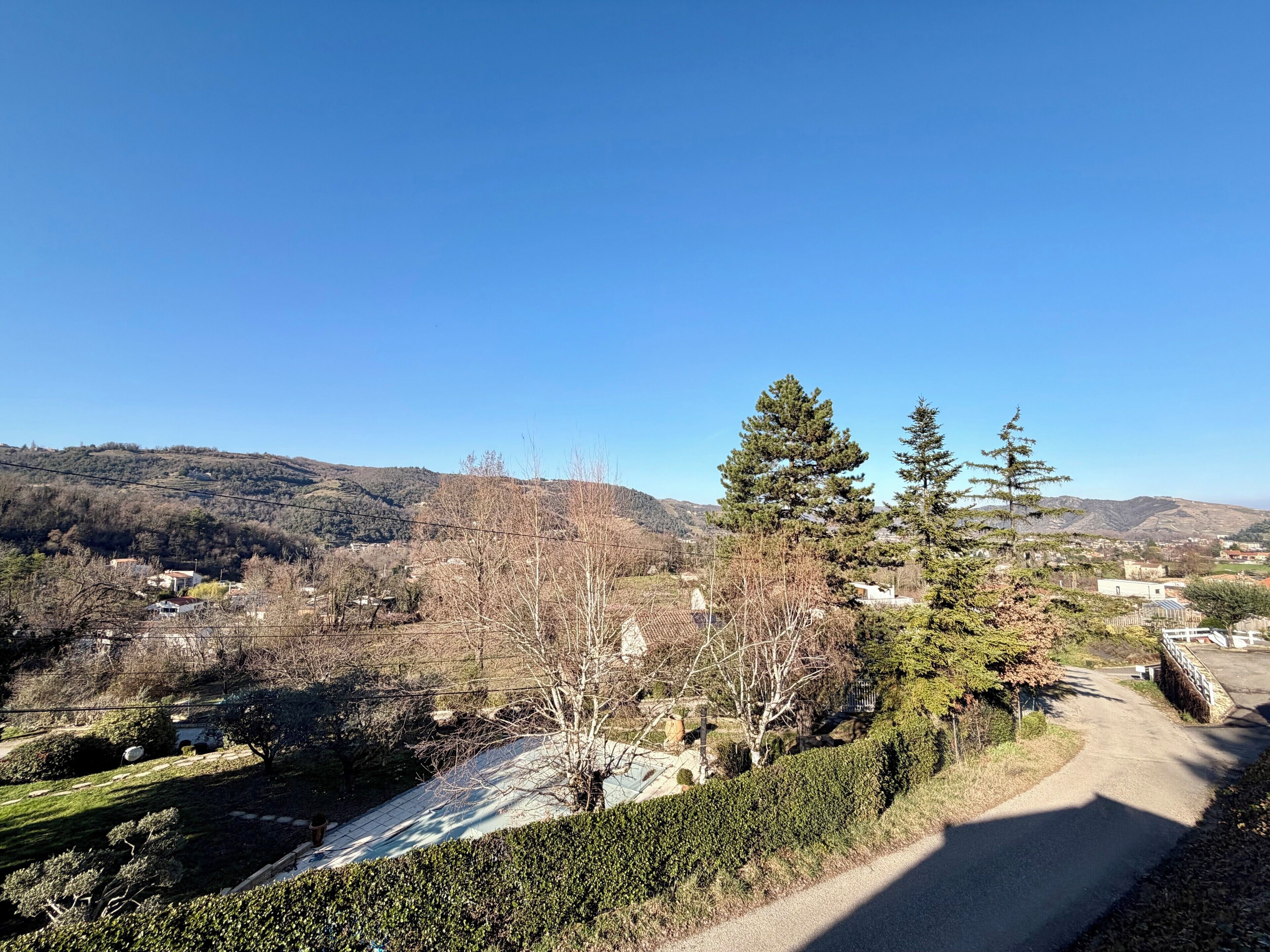 A rural landscape with a clear sky, a paved path, and scattered buildings.