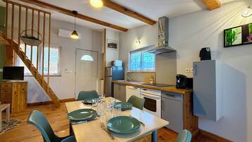Een eetgedeelte met een houten tafel voor vier personen, een keuken met moderne apparatuur, en een trap naar een hoger gelegen verdieping.