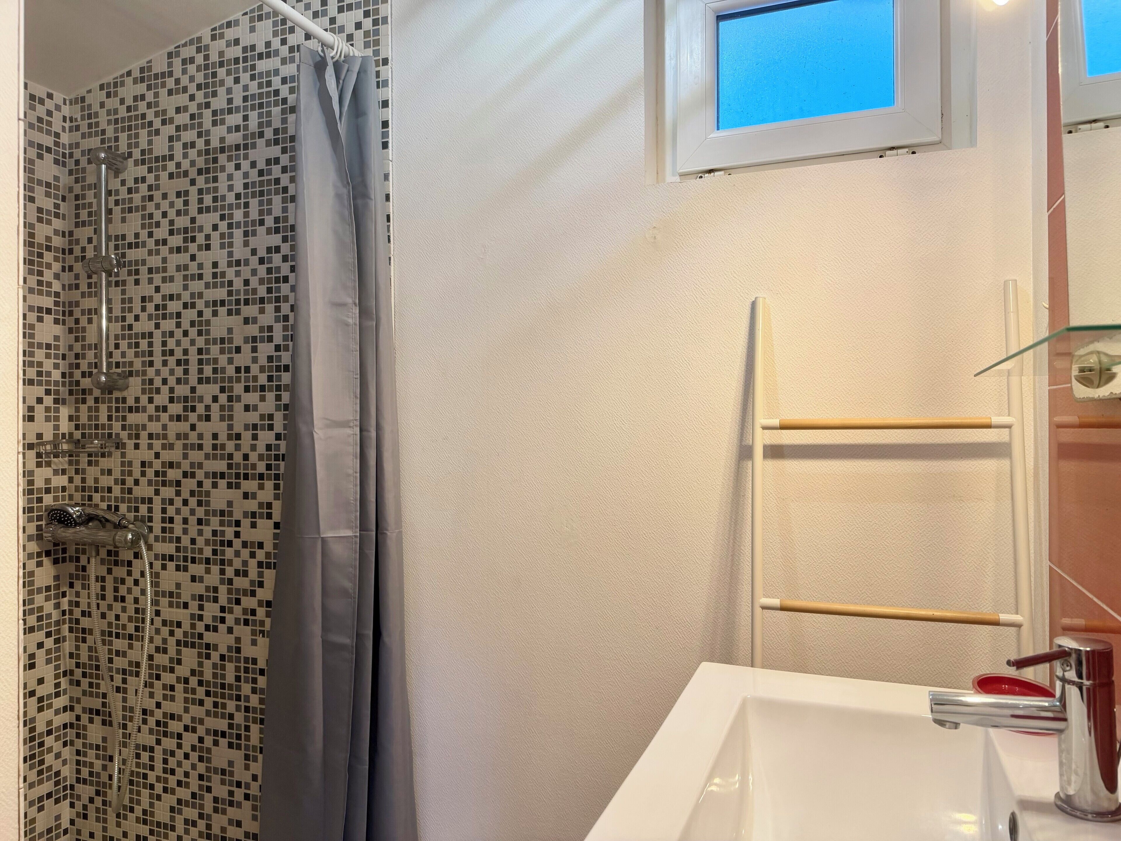 A bathroom with a shower, a sink, a window, and a towel rack.