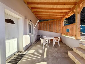 Ein überdachter Patio-Bereich mit Holzboden, einer weißen Tür und einem kleinen Tisch mit Stühlen.