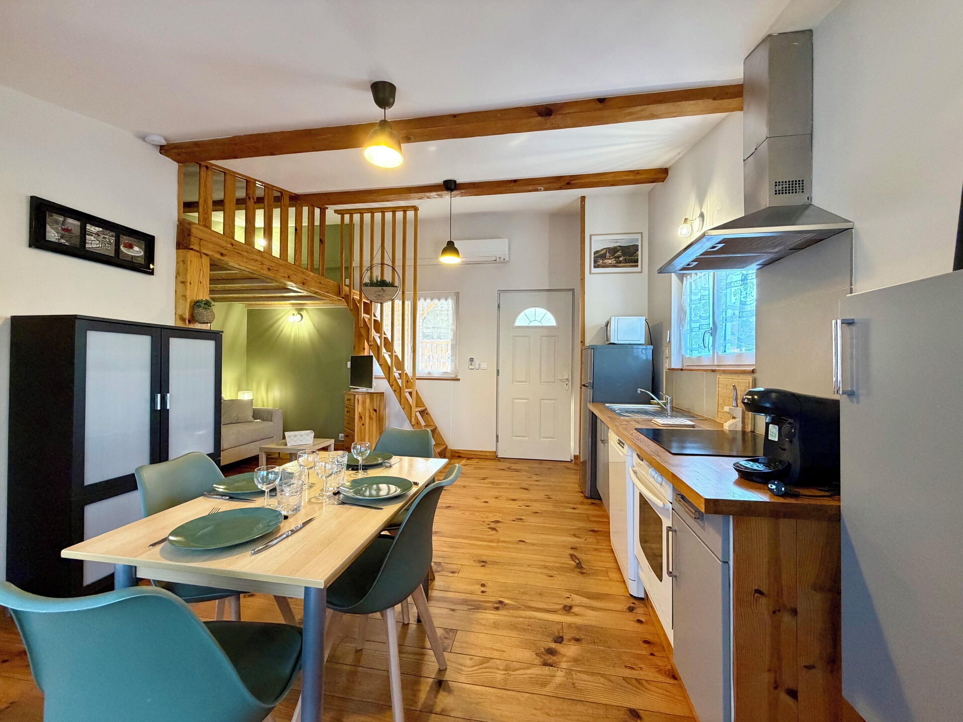 Cocina compacta con piso de madera, zona de comedor con una mesa dispuesta para dos personas, y una escalera que sube a un nivel superior.