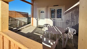 A covered outdoor area with a wooden bench, a table with chairs, a door, and a window with patterned glass.