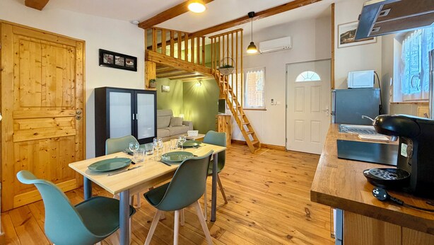 A wooden interior with a dining table set for four, a staircase, and a kitchen area with a coffee machine.