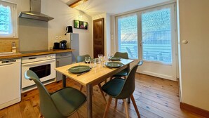 A kitchen with a dining area, wooden flooring, and a large window with patterned blinds.