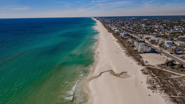 Eine Küstenstadt mit einem breiten Sandstrand, einem klaren blauen Meer und Wohnhäusern entlang der Küste.