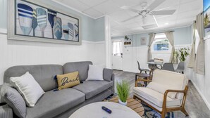 Ein Wohnzimmer mit grauem Sofa, rundem Couchtisch, weißem Sessel, Deckenventilator und einem Bild von Schlägern.