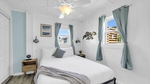 Ein Schlafzimmer mit einem Bett, einem Nachttisch, einem Wandleuchten, einem Deckenventilator und einem Fenster mit Vorhängen.